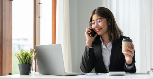 Young woman using mobile phone while sitting on table