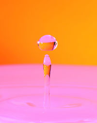 Close-up of drop falling in pink water against orange background