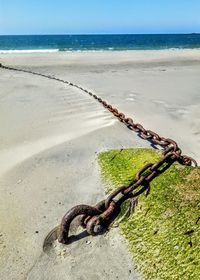 Rusty metal chain on beach against sky