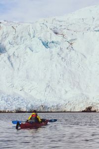 Man rowing boat in river against sky during winter