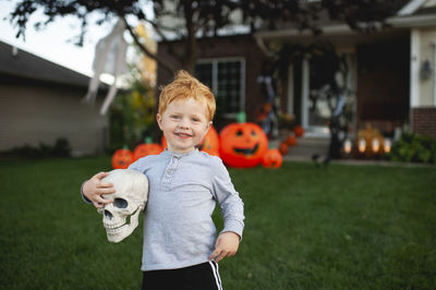 Toddler boy smiling while holding halloween decor in front yard