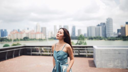 Full length of smiling young woman standing against cityscape