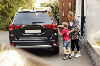 Mother and son charging electric car by house