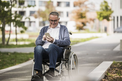 Smiling senior man using smart phone sitting on wheelchair