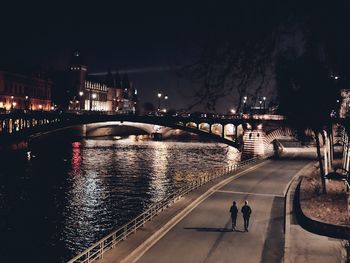 People walking on bridge over river in city at night