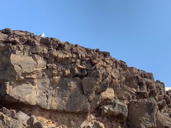 Low angle view of rocks against clear blue sky