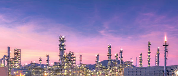 Panoramic view of illuminated factory against sky at sunset