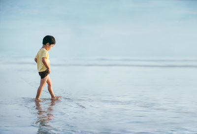 Boy standing on beach against sky