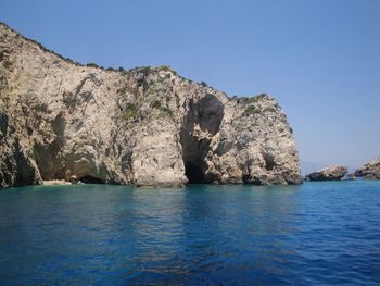 Rock formation in sea against clear blue sky