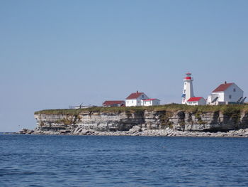 Lighthouse by sea against clear sky