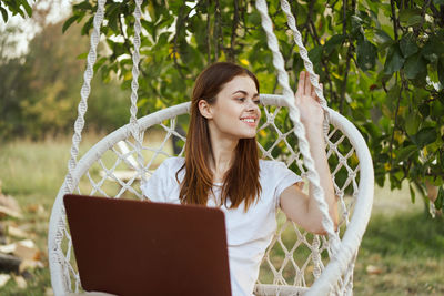 Portrait of smiling young woman using laptop at park