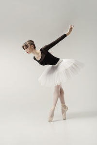 A ballerina in a bodysuit and tutu poses in motion showing ballet elements while standing on pointes