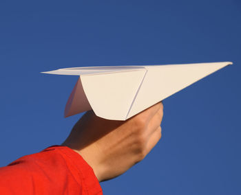 Low section of person holding paper against blue sky