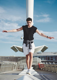 Young man with arms outstretched standing against sky