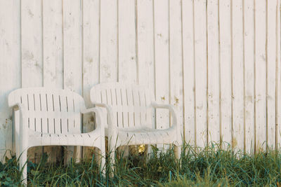 Empty chairs on grass against wooden wall