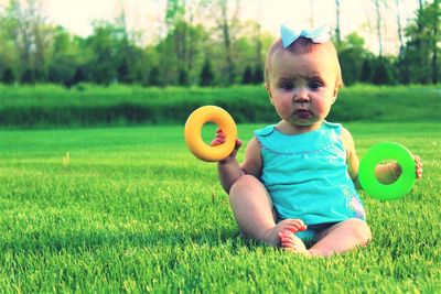 Full length portrait of cute baby girl holding plastic rings on grassy field