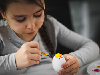 A little caucasian girl enthusiastically paints an easter egg with a brush with acrylic paint