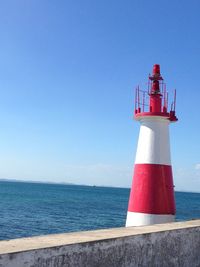 Lighthouse by sea against clear blue sky