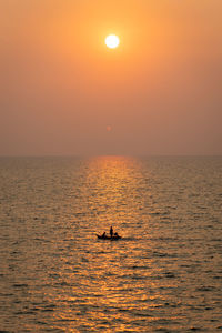 Silhouette people in sea against sky during sunset