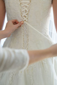 The bridesmaid laces up the bride's white wedding dress on her wedding day