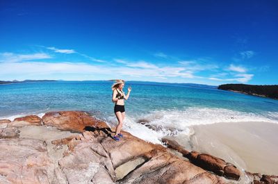 Woman standing on rock at beach against sky