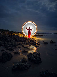 Man standing on rock at beach against sky during sunset