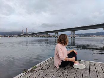 Woman sitting on bridge over river against sky