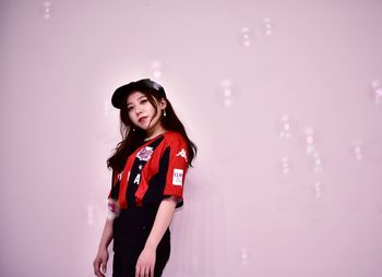 Portrait of young woman standing against red wall