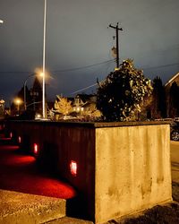 Illuminated street amidst buildings against sky at night