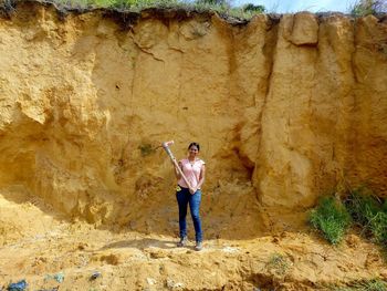 Full length of woman holding pick standing against rock