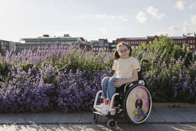 Smiling girl sitting in wheelchair in front of flowering plants