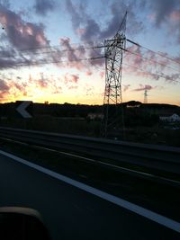 Electricity pylon by road against sky at sunset