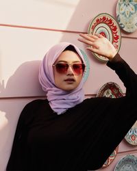 Portrait of young woman wearing sunglasses and headscarf against wall