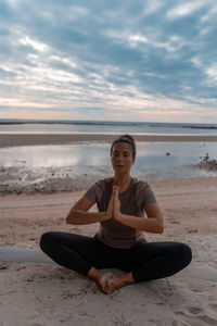 Portrait of young woman sitting at beach against sky