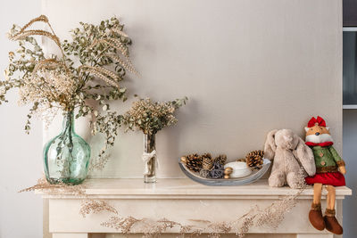 Dried branches of plants in glass vases and cones in bowl near toys decorating fireplace for christmas