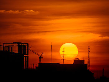 Silhouette cranes and buildings against sky during sunset