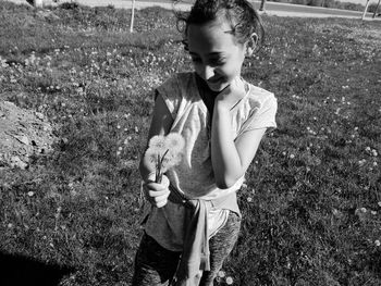 Smiling girl holding dandelions while standing on field