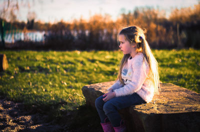 Side view of thoughtful girl on seat at field