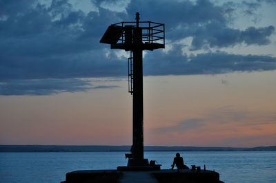 Silhouette cross by sea against sky at sunset