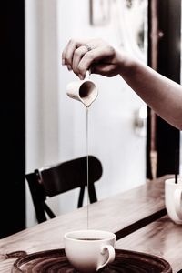 Cropped hand pouring honey in cup on table