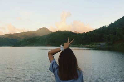 Rear view of woman with peace sign standing by lake