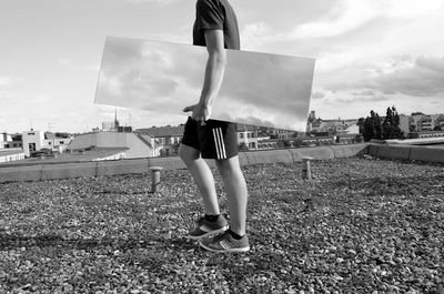 Low section of young man carrying mirror while walking on building terrace