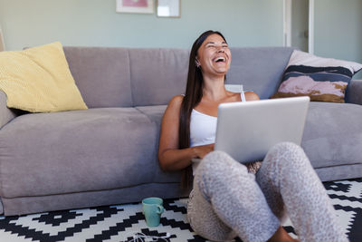 Young woman using phone while sitting on sofa at home