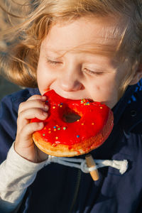 Girl in delight eats donut with red icing, food stained her mouth