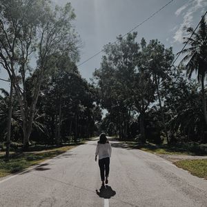 Rear view of woman walking on road amidst trees