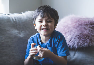 Portrait of happy boy holding medicine and water while sitting on sofa at home