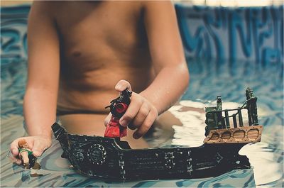 Midsection of shirtless boy playing with toy while sitting in swimming pool