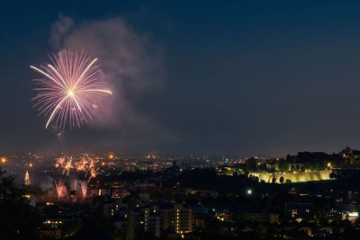 Firework display over city against sky at night