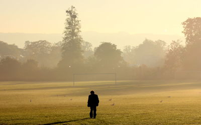 Rear view of man walking on playing field in foggy weather