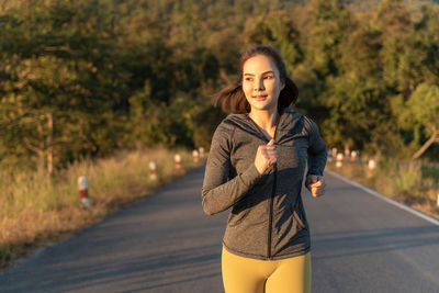 Happy attractive young woman wearing her warm up jacket while running at a local park